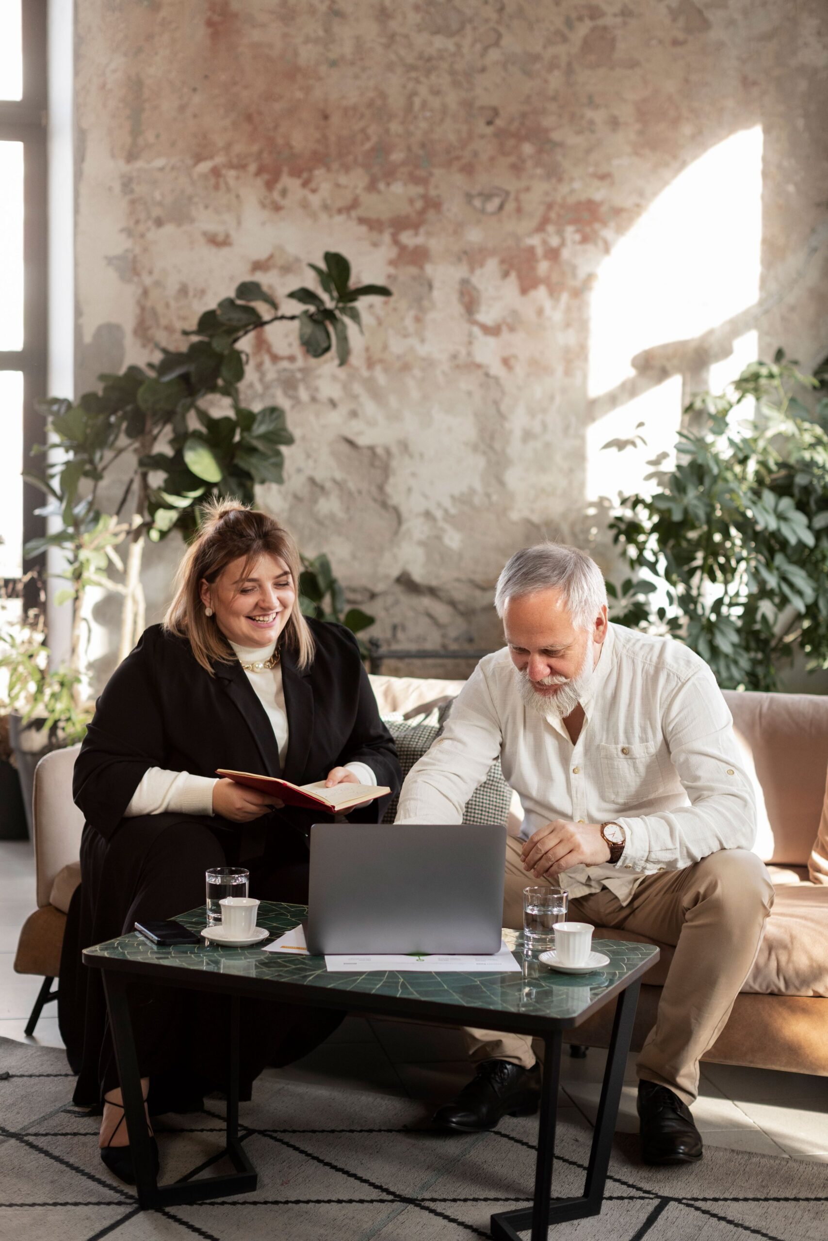 A woman and an older gentleman sitting in a modern office looking at a laptop on a coffee table