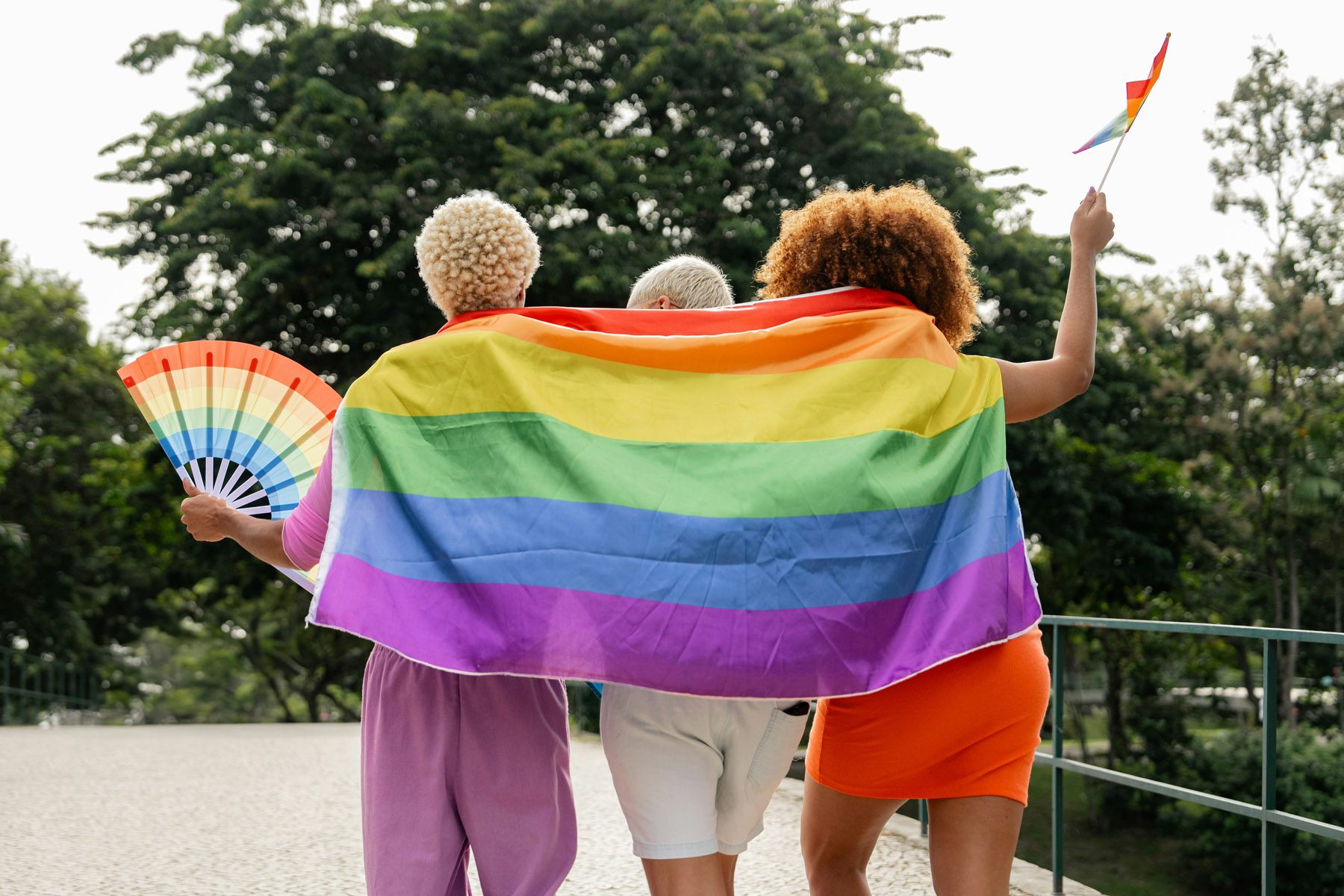 Three people standing together at a Pride festival with a Pride flag draped around their shoulders